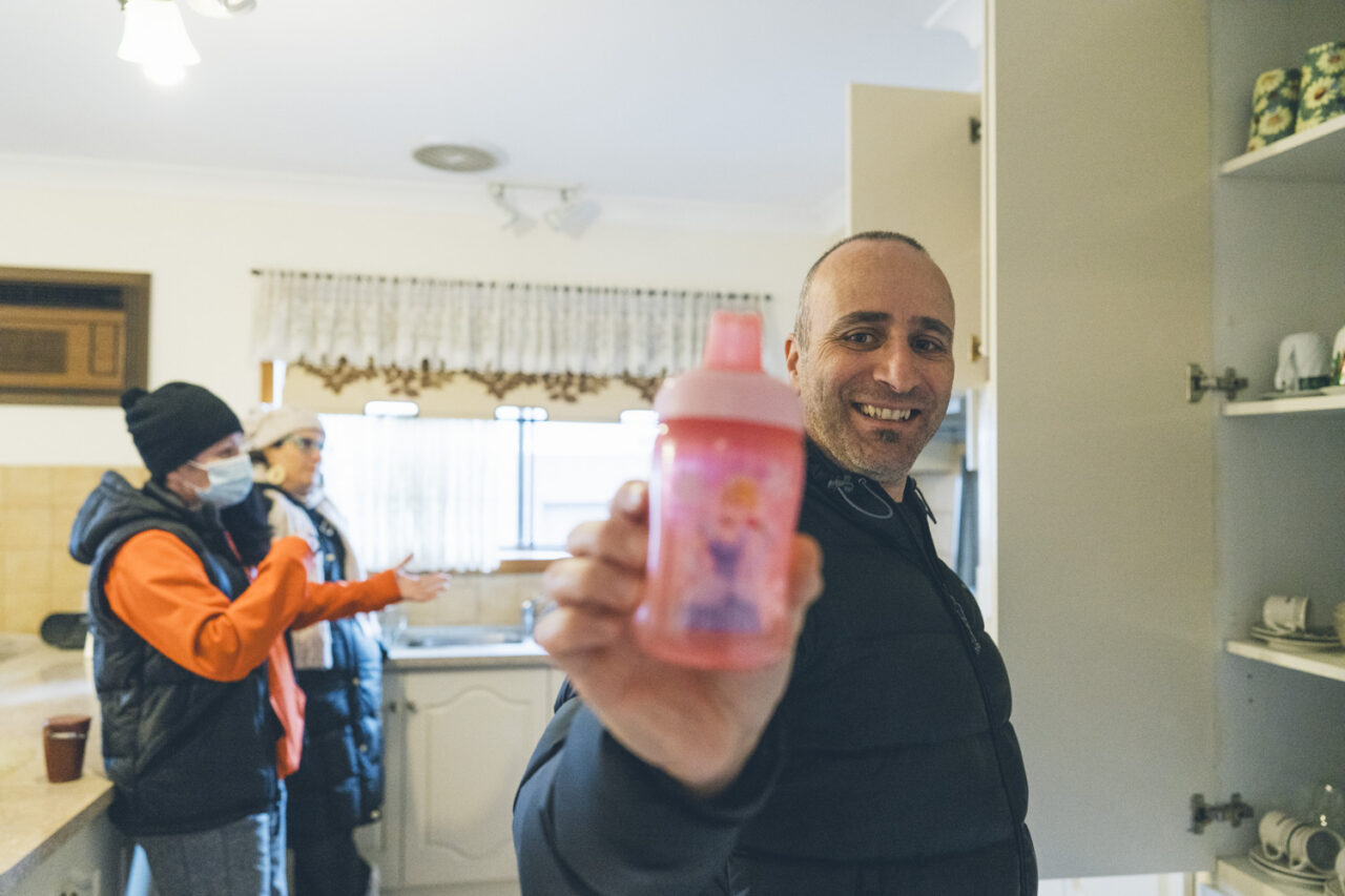 Family member smiling and holding a child's drink bottle found in the kitchen during a deceased estate photography session