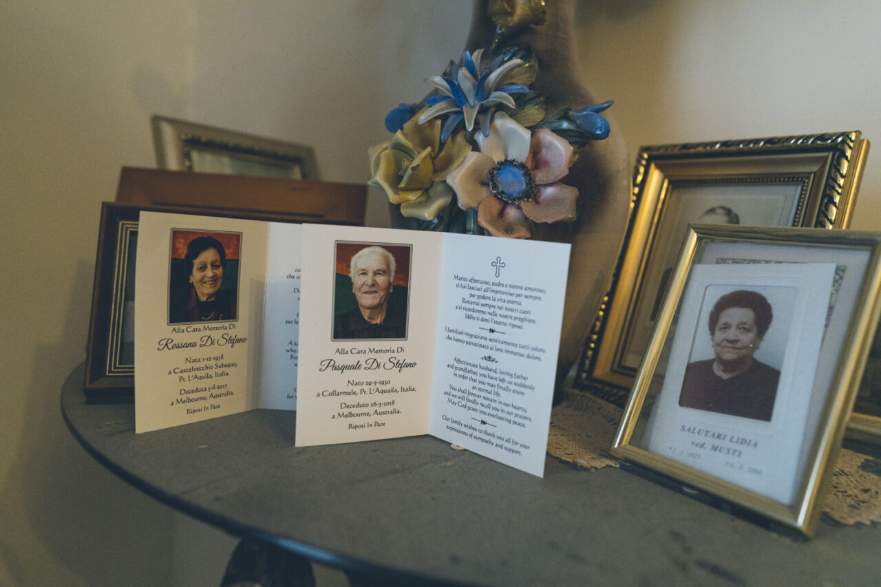 Memorial cards for two family members displayed alongside framed photographs on a table, documented during a deceased estate photography session in Melbourne