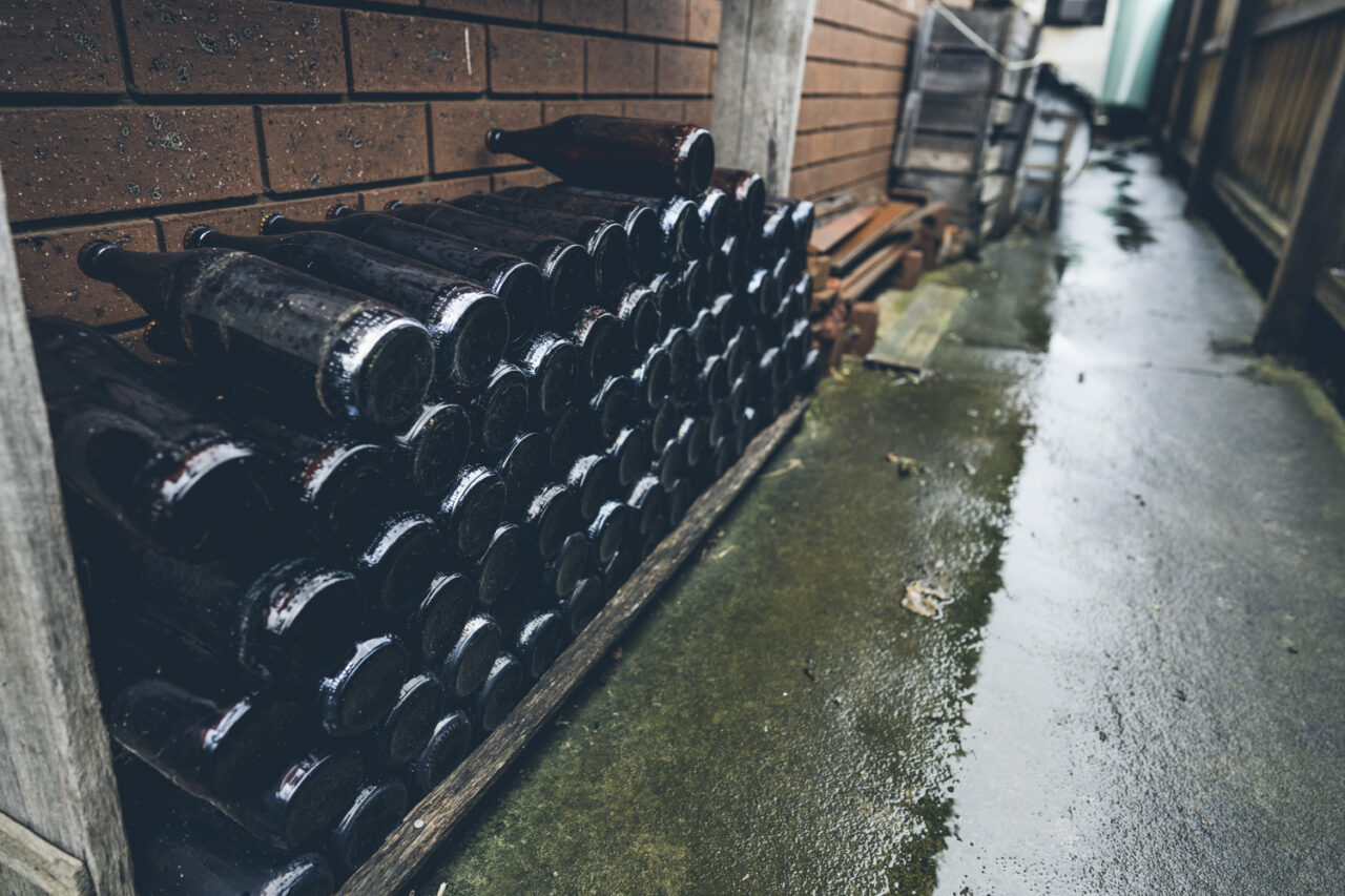 Rows of old dusty wine bottles stored in a rack outside against a brick wall, photographed during a deceased estate session in Melbourne