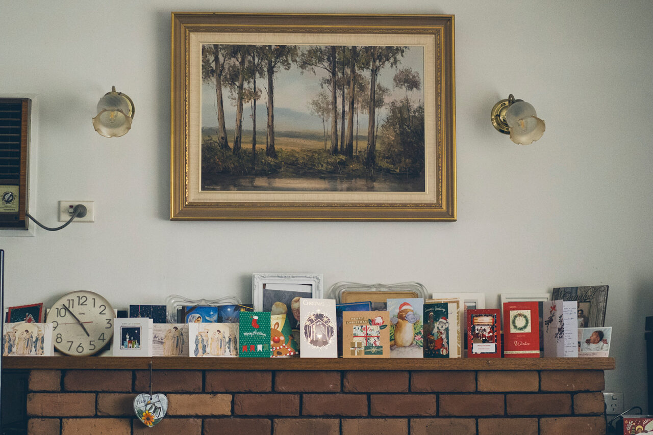 Mantelpiece lined with Christmas cards and a clock, with a landscape painting above, documentary family home photography