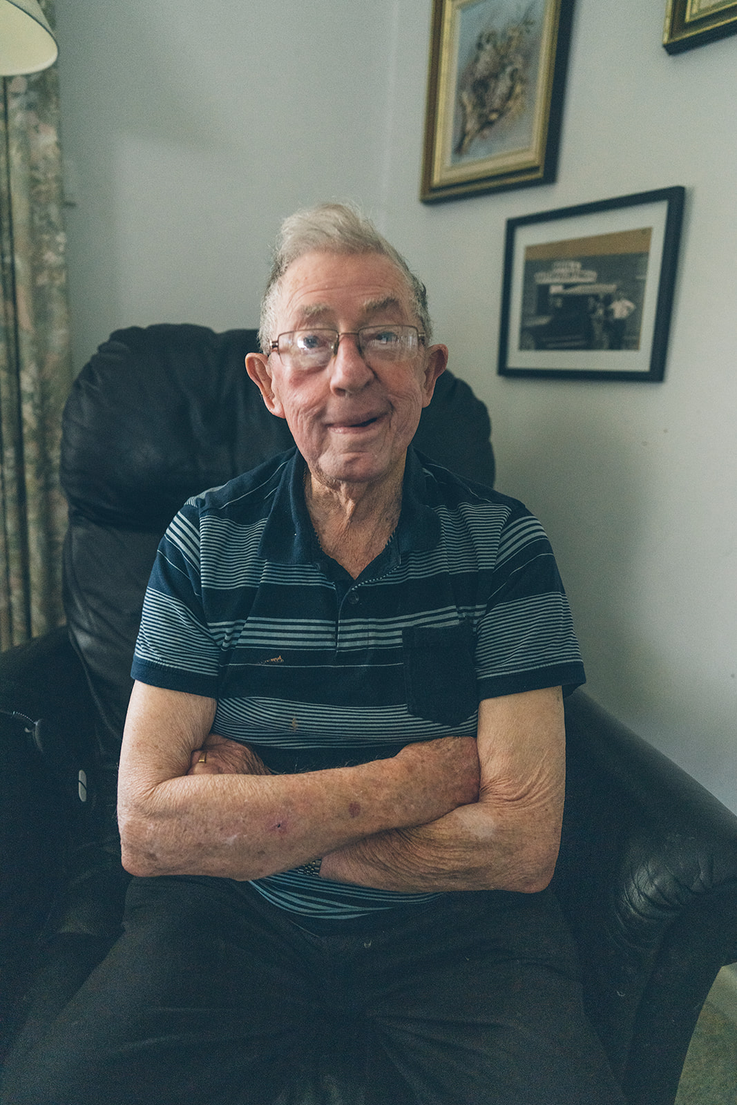 ortrait of an elderly man sitting with arms crossed and smiling in his family home lounge chair, documentary photography Melbourne