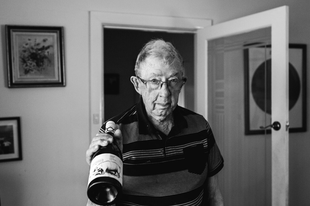 Black and white portrait of an elderly man holding a bottle of scotch in his family home, documentary photography Melbourne