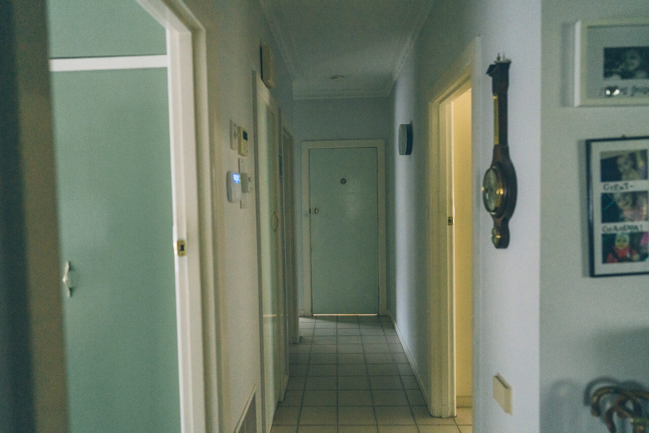 Long hallway of a family home with a barometer on the wall and family photographs at the end, documentary photography Melbourne
