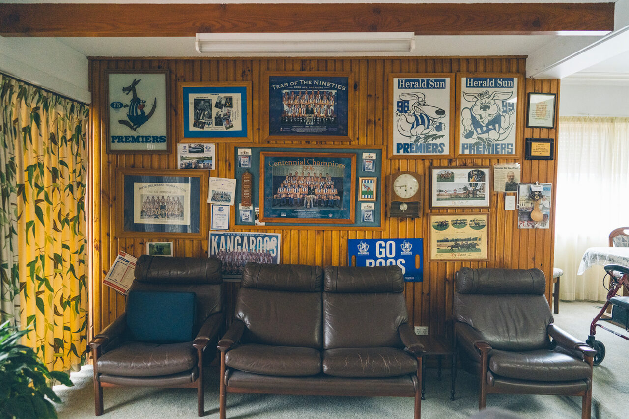 Living room wall covered in North Melbourne AFL football memorabilia and framed posters, documentary family home photography Melbourne