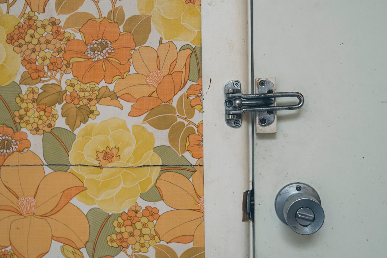 Vintage orange floral wallpaper beside a door latch, detail photograph from a documentary family home session in Melbourne