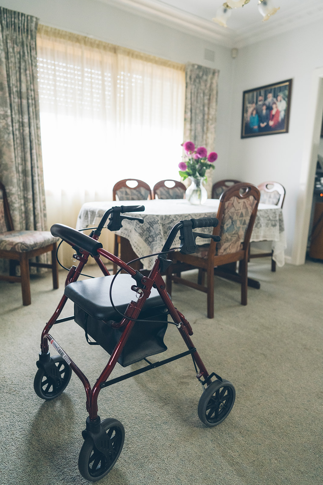 Walking frame in a dining room with a lace tablecloth and fresh flowers, documentary family home photography Melbourne