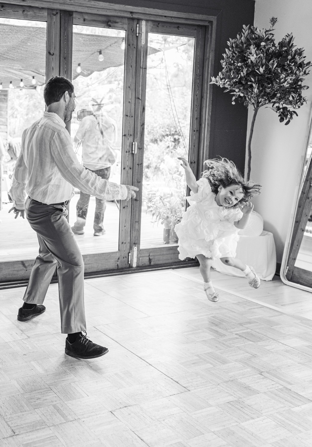 Black and white image of a man spinning a young girl in a white dress on a dance floor, her hair flying out as she grins