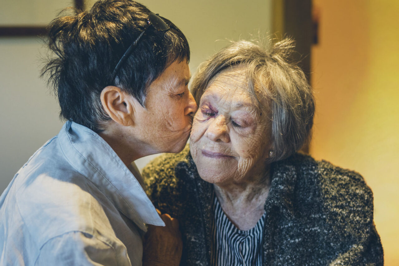 Candid documentary photograph of a person kissing an elderly woman on the cheek, captured during a family portrait session by LJM Photography Melbourne