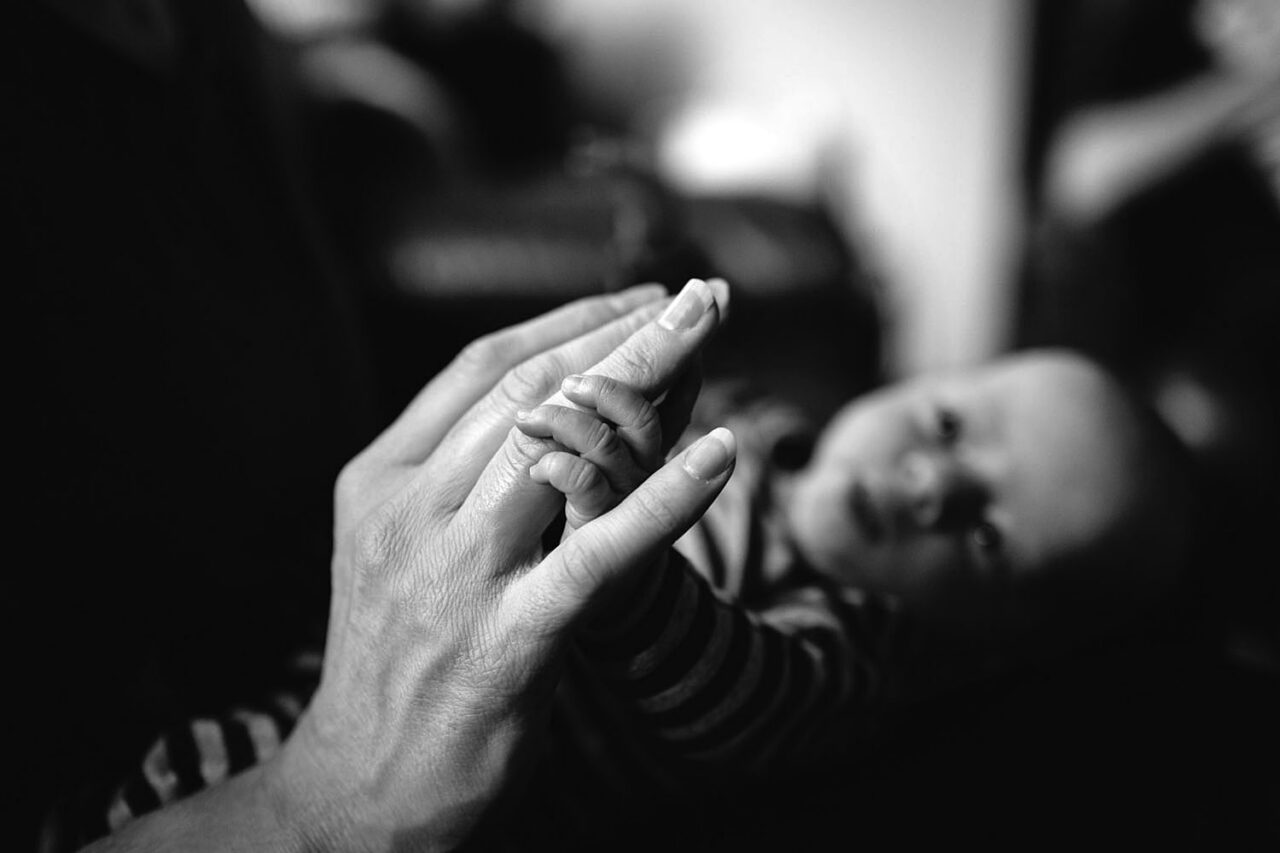 Black and white close up of two pairs of hands touching fingers with a smiling person softly out of focus in the background, documentary portrait photography by LJM Photography Surf Coast Melbourne
