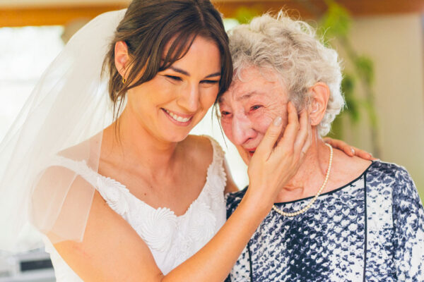 Bride in her grandmother's vintage wedding dress pressing her cheek against her emotional grandmother who wipes away tears, captured during a backyard wedding on the Surf Coast by LJM Photography