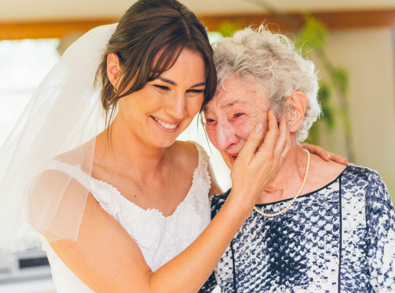 Bride in her grandmother's vintage wedding dress pressing her cheek against her emotional grandmother who wipes away tears, captured during a backyard wedding on the Surf Coast by LJM Photography