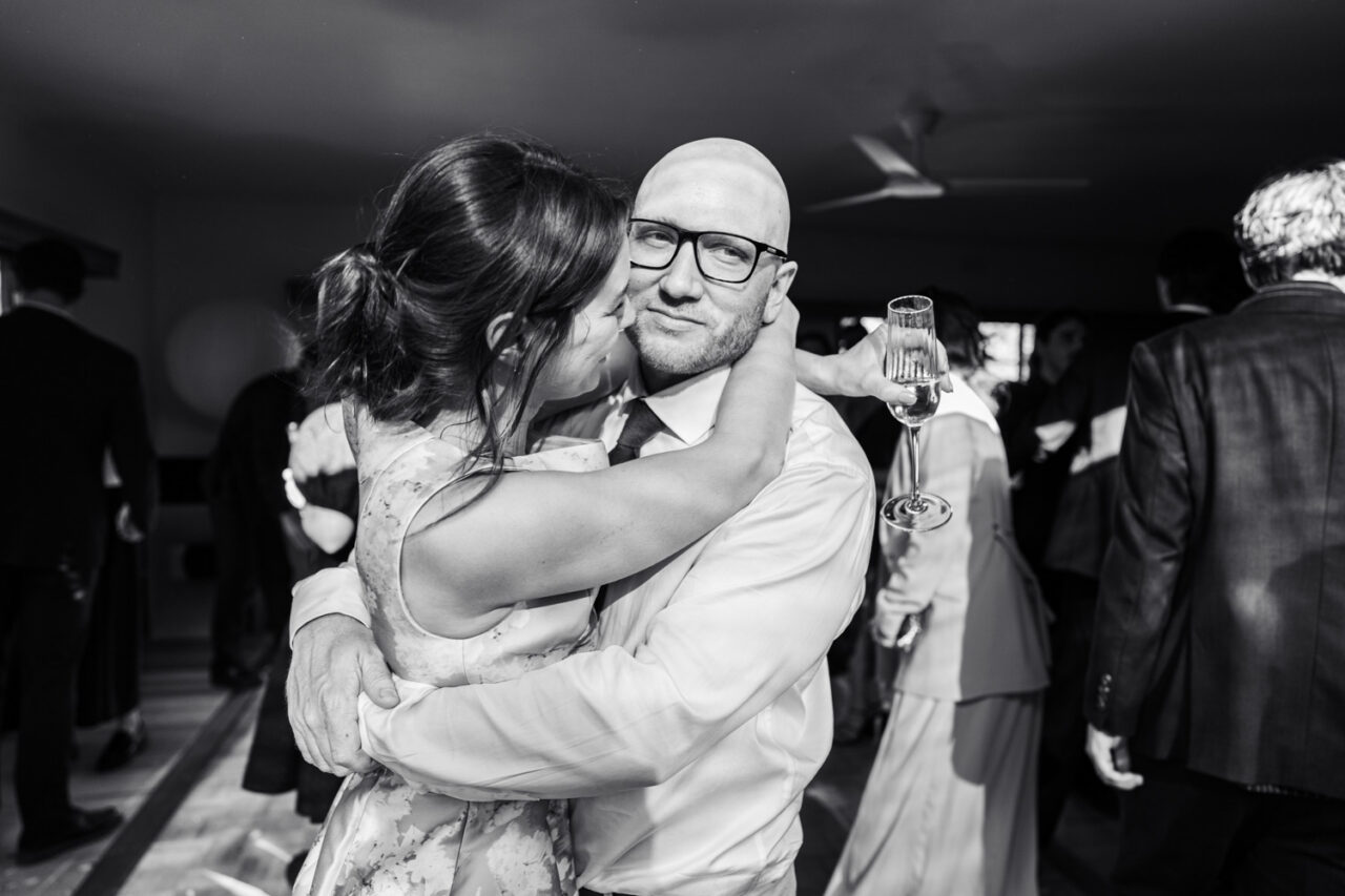Black and white image of a bride and groom slow dancing at their backyard wedding reception, the groom looking directly at the camera with a quiet smile