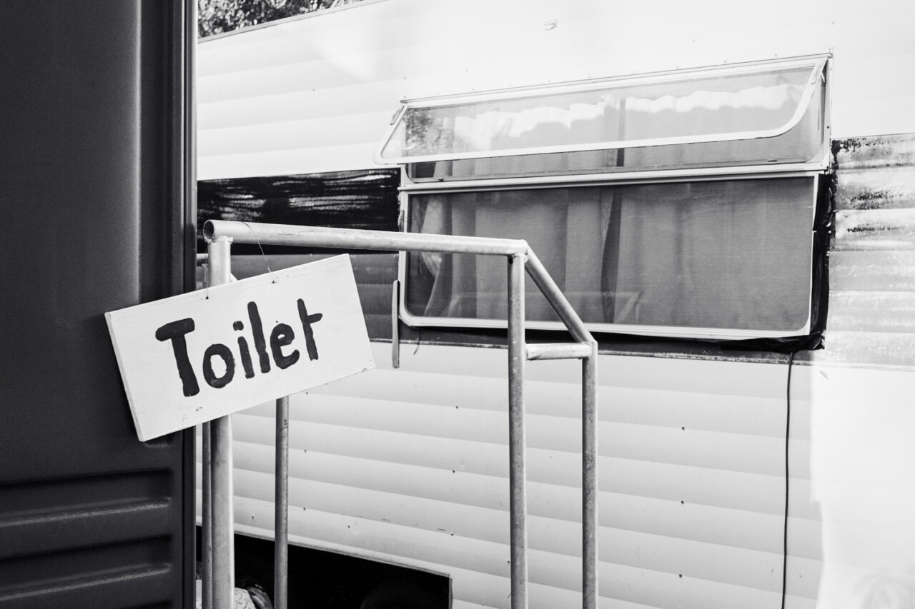 Black and white image of a handmade cardboard toilet sign attached to a vintage caravan at a DIY backyard wedding on the Surf Coast