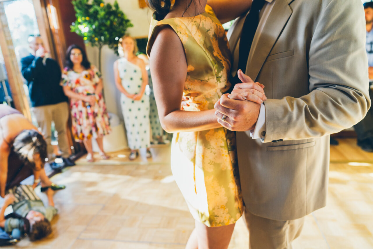 Groom lifting a large slice of layered chocolate wedding cake from Ginger and Spice while a child watches eagerly beside homegrown flower arrangements