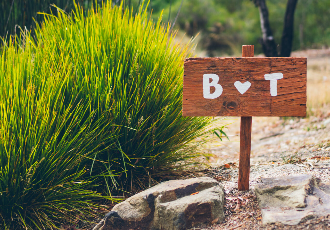 Handmade wooden wedding sign with the initials B and T painted in white, set among native grasses on the Surf Coast Caption: A handmade sign, a backyard, and a day built from scratch.