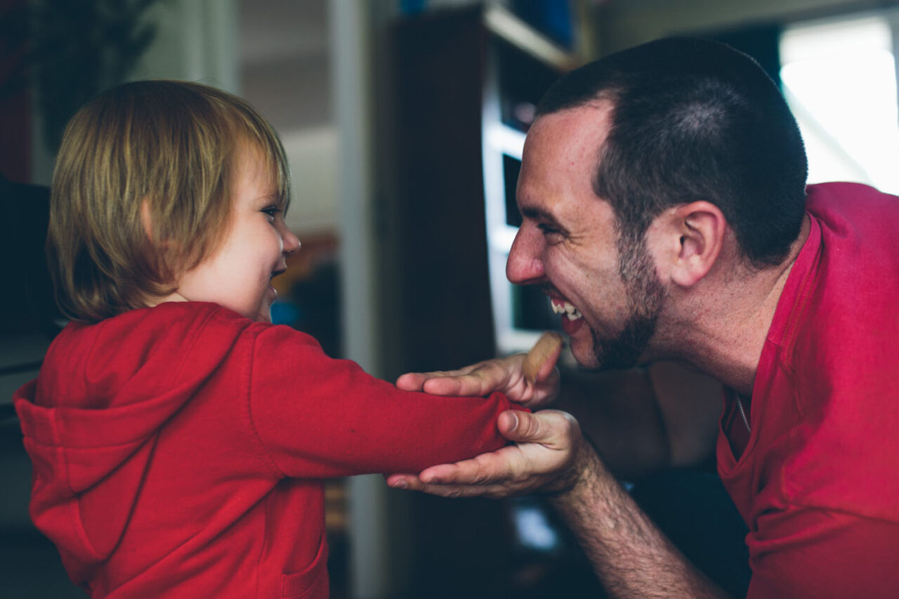 A father and toddler laughing face to face, both in red, captured by LJM Photography