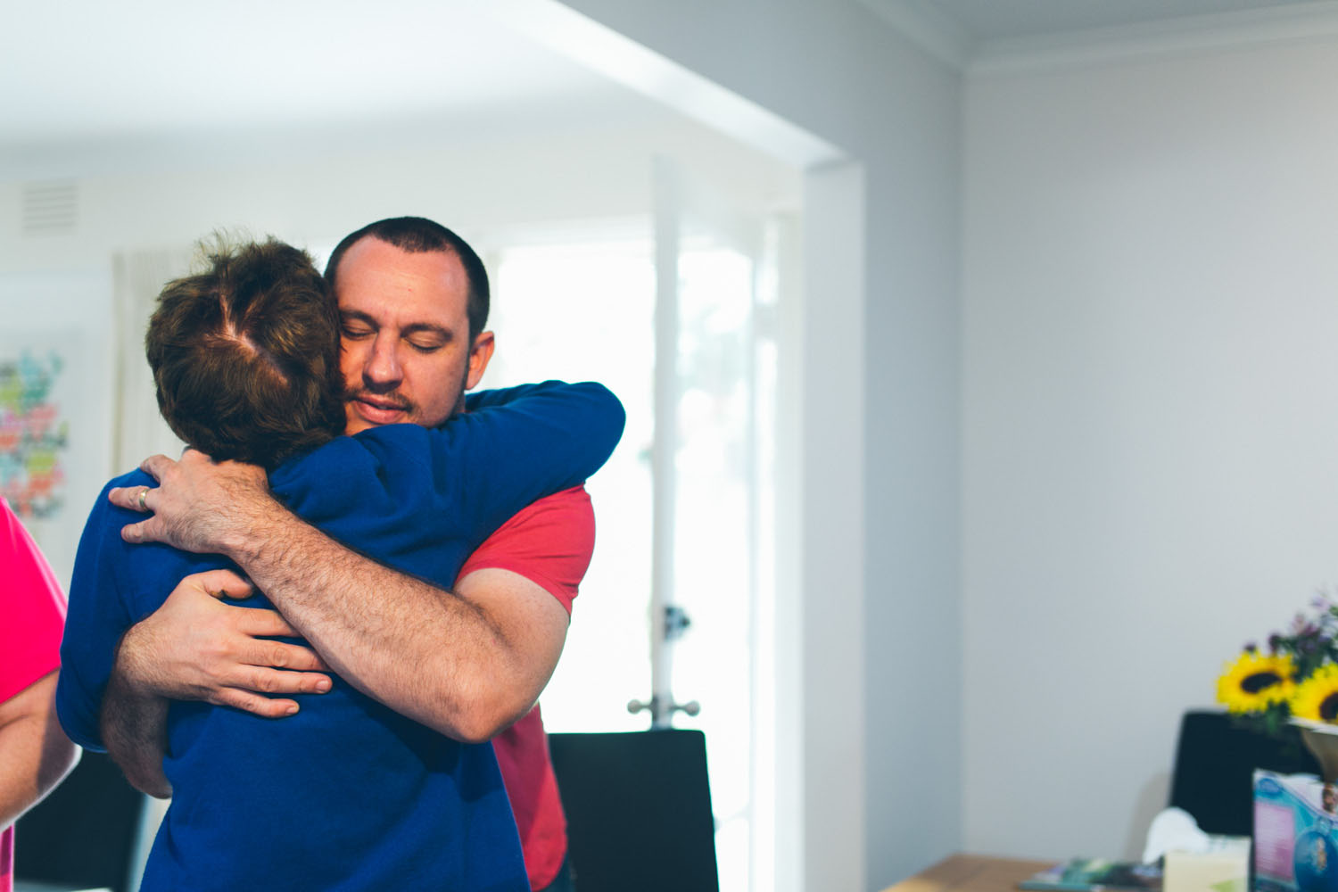 A man holding a woman in a long embrace with eyes closed, sunlit room, documentary family photography by LJM Photography