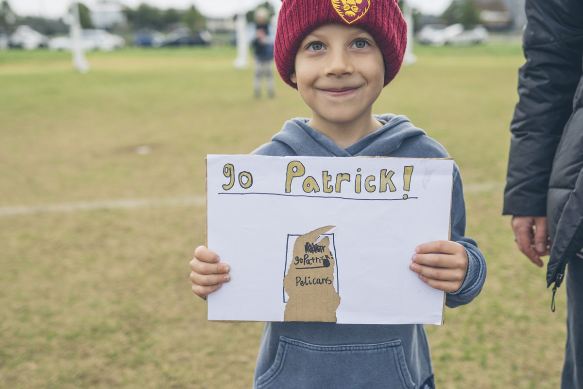Young boy holding a handmade sign cheering on a player at a junior soccer match