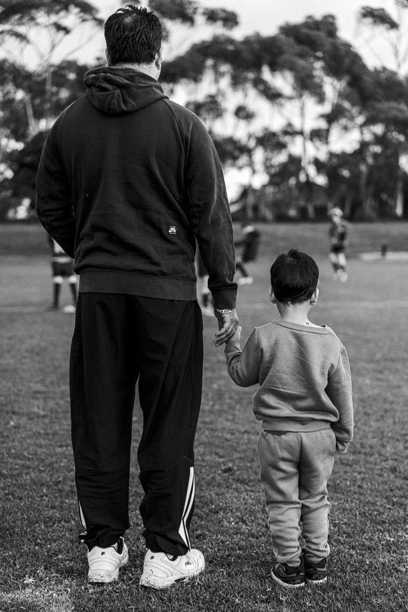 Father and young son holding hands walking across a soccer ground, black and white