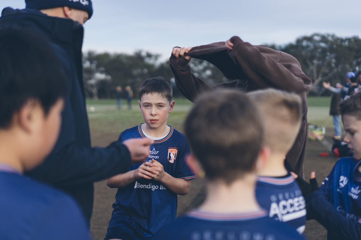 Junior soccer player listening intently during a coach's team talk making eye contact with the camera