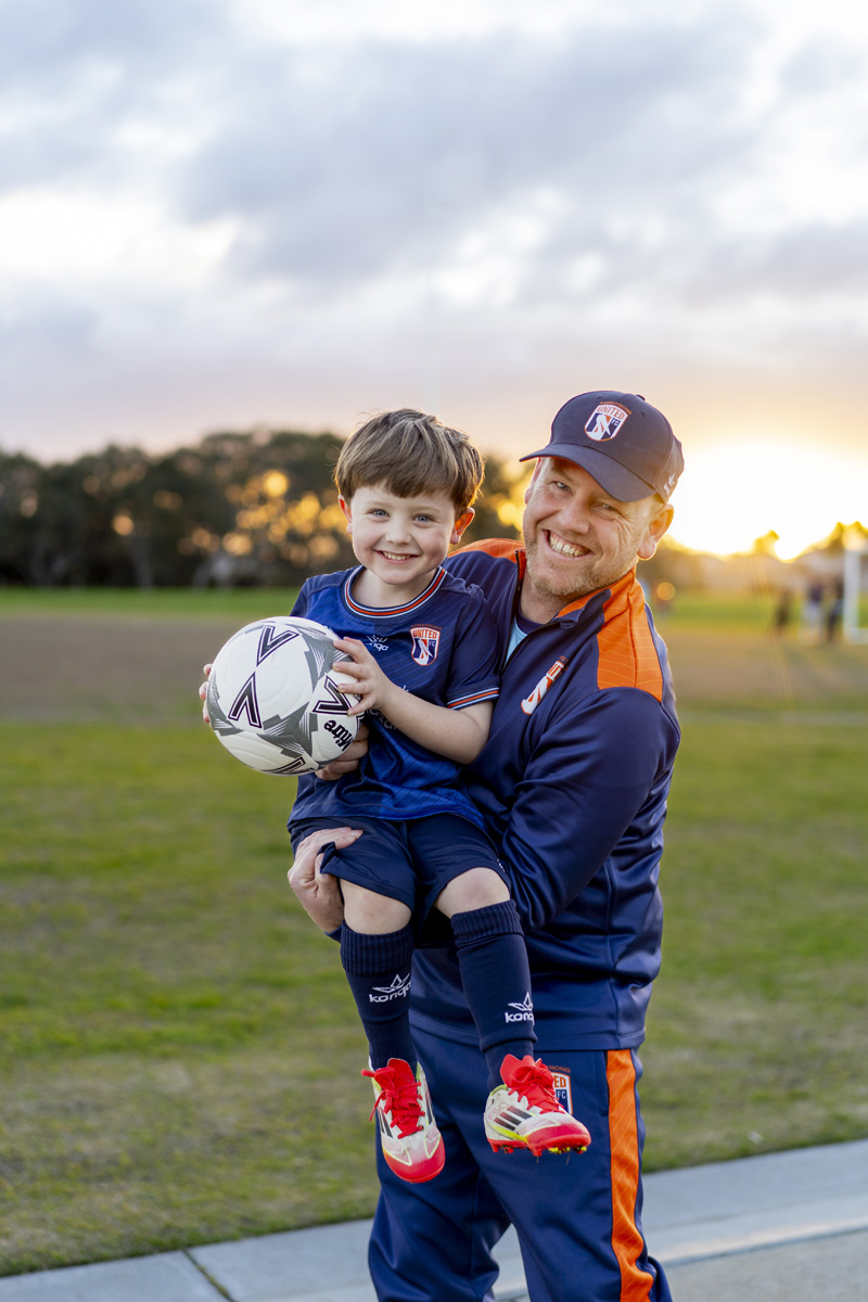 Family soccer photo of Father holding his young son with a soccer ball at sunset on a Surf Coast oval
