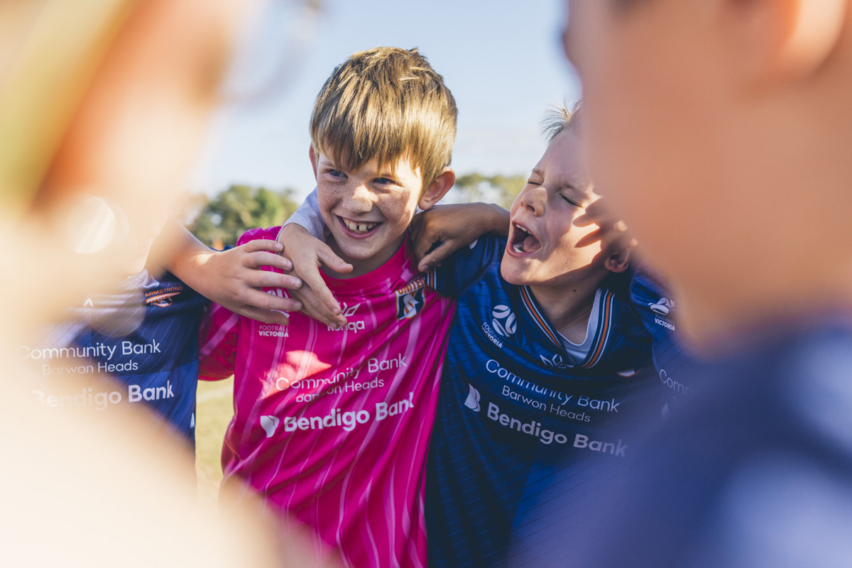 Junior soccer players laughing with arms around each other after a match