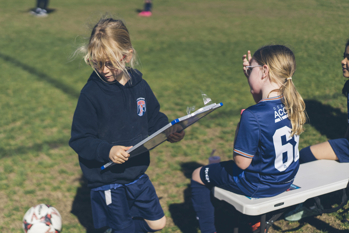Two girls soccer players looking at a clipboard on the sideline