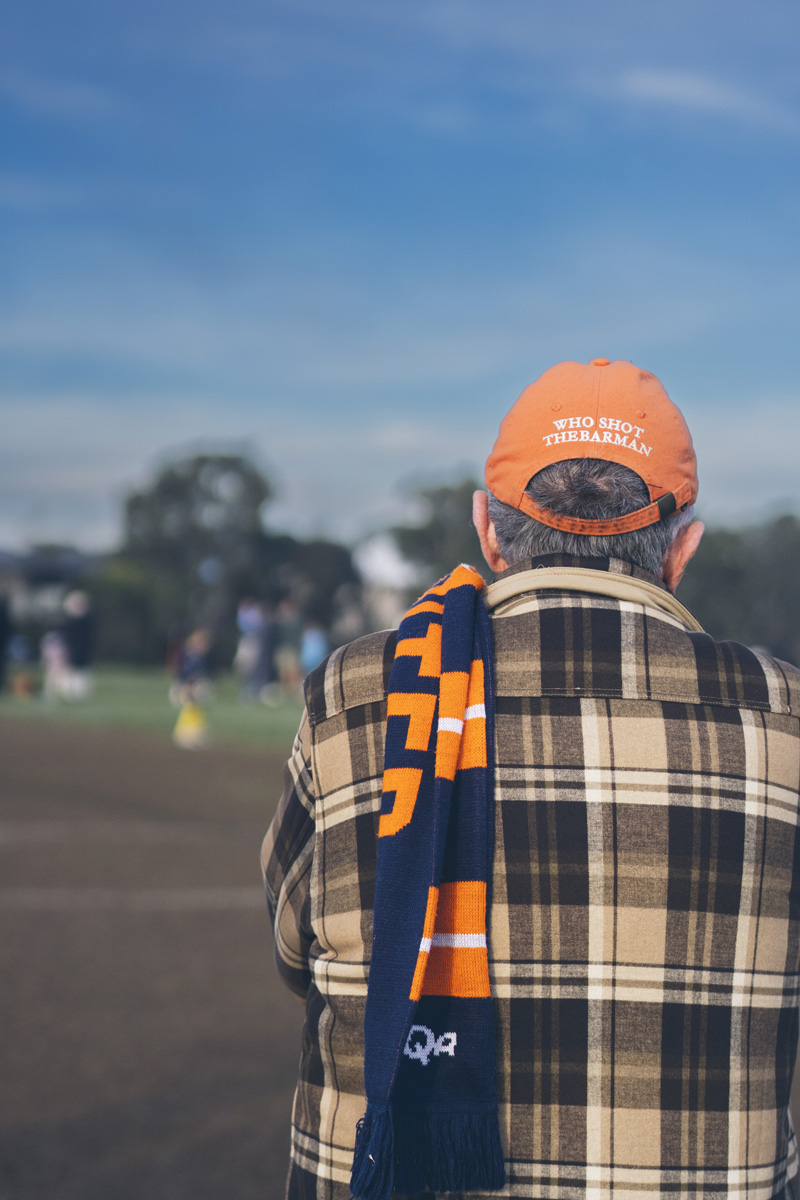Older supporter watching a soccer match wearing a club scarf, back turned