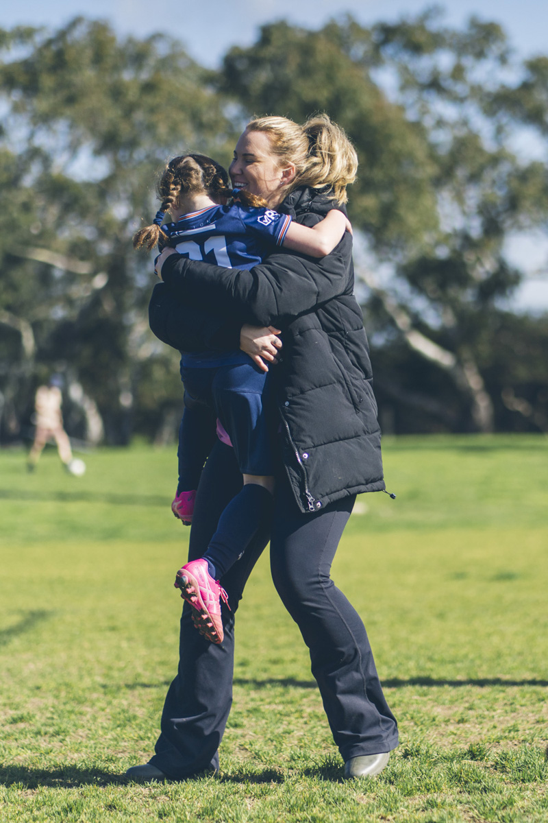Mother lifting and hugging her daughter in soccer uniform on the field
