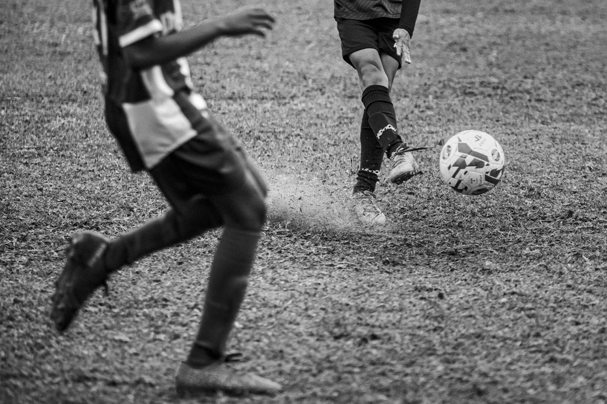 Close up of junior soccer players' legs and a ball kicking up dust