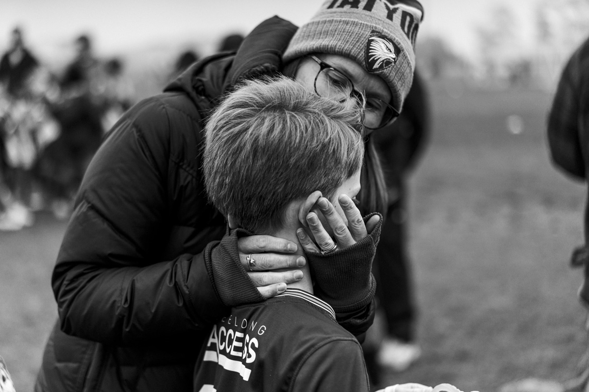 Parent comforting a young soccer player on the sideline, black and white