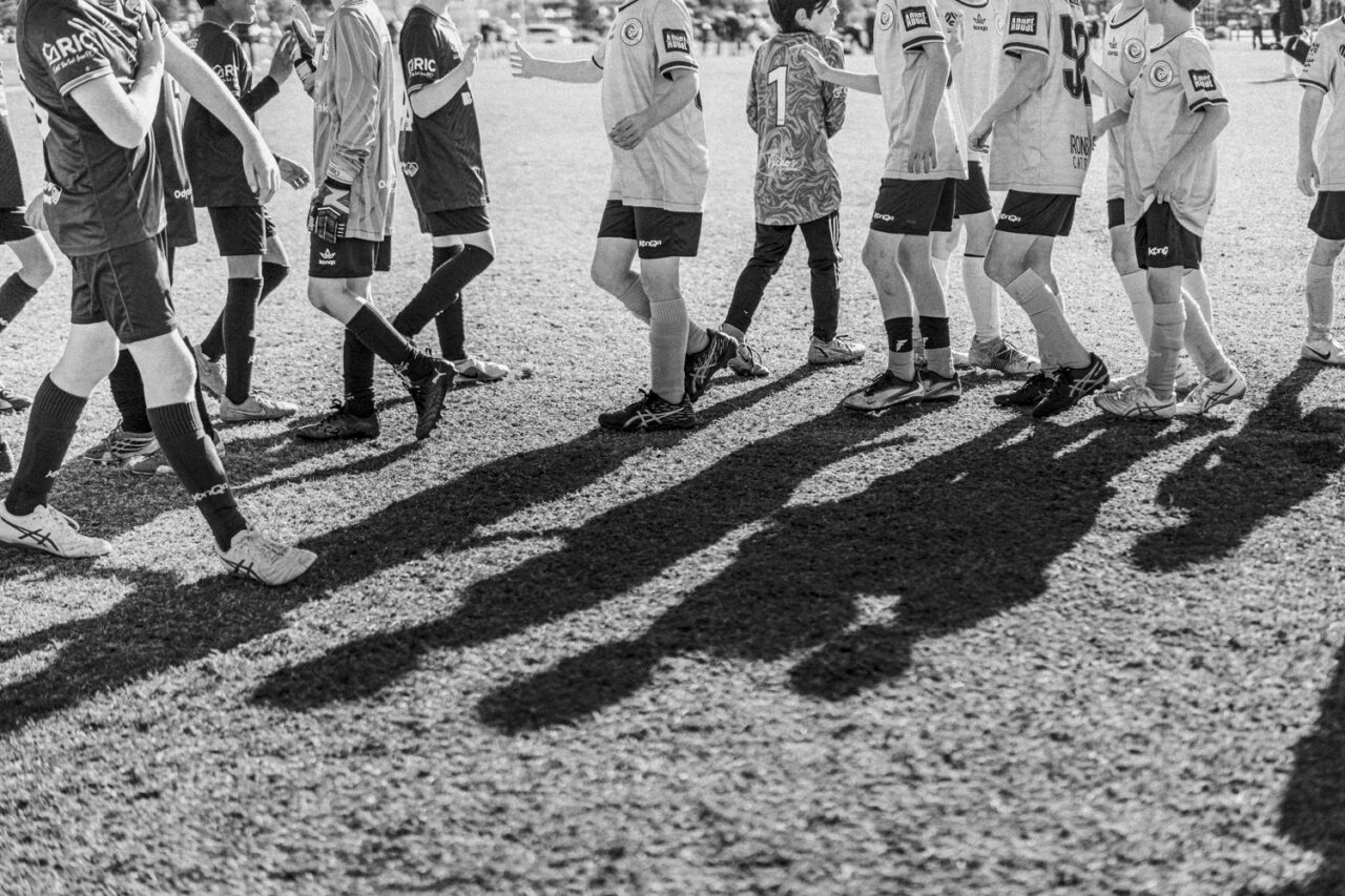 Junior soccer players shaking hands after a match, long shadows, black and white