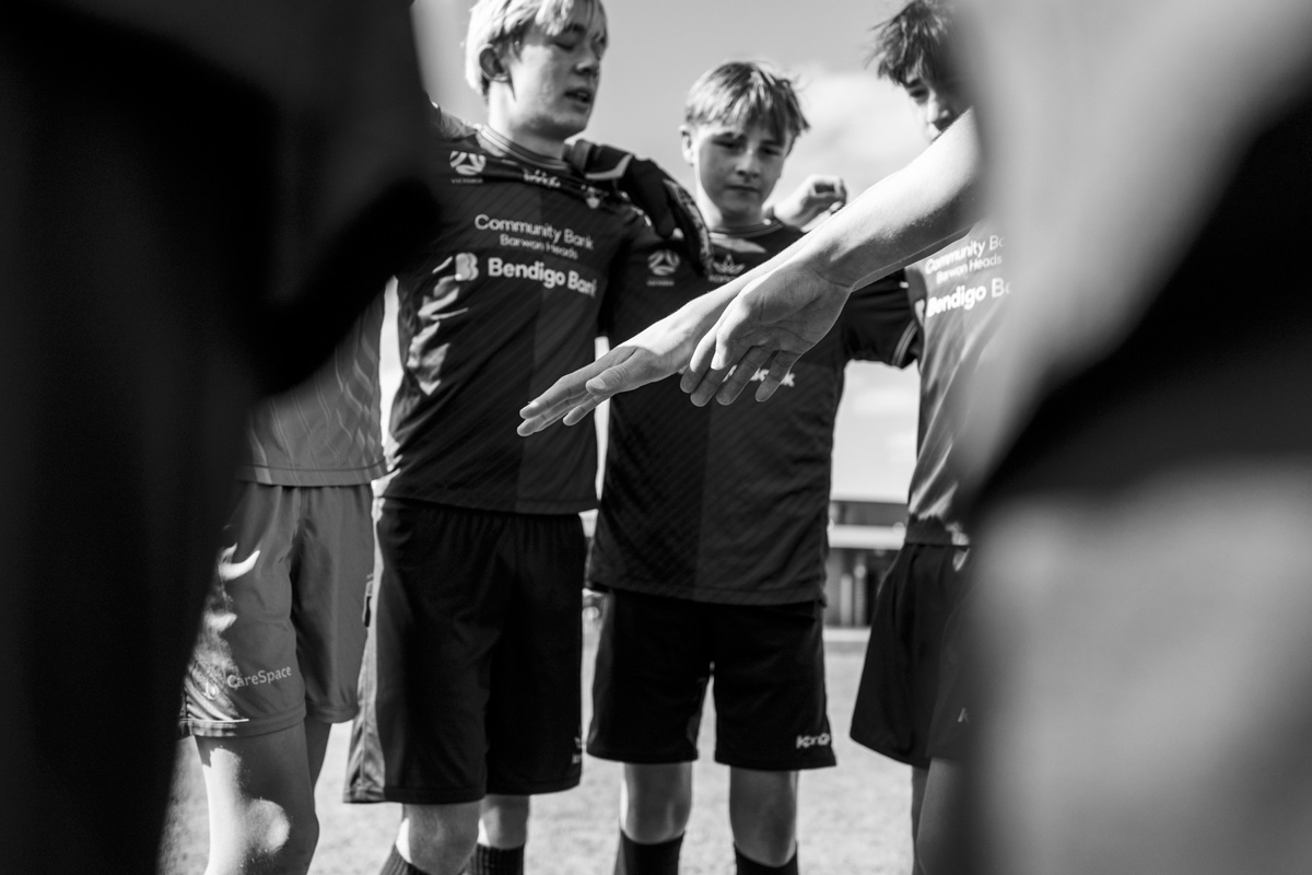 Junior soccer team stacking hands together in a huddle, black and white