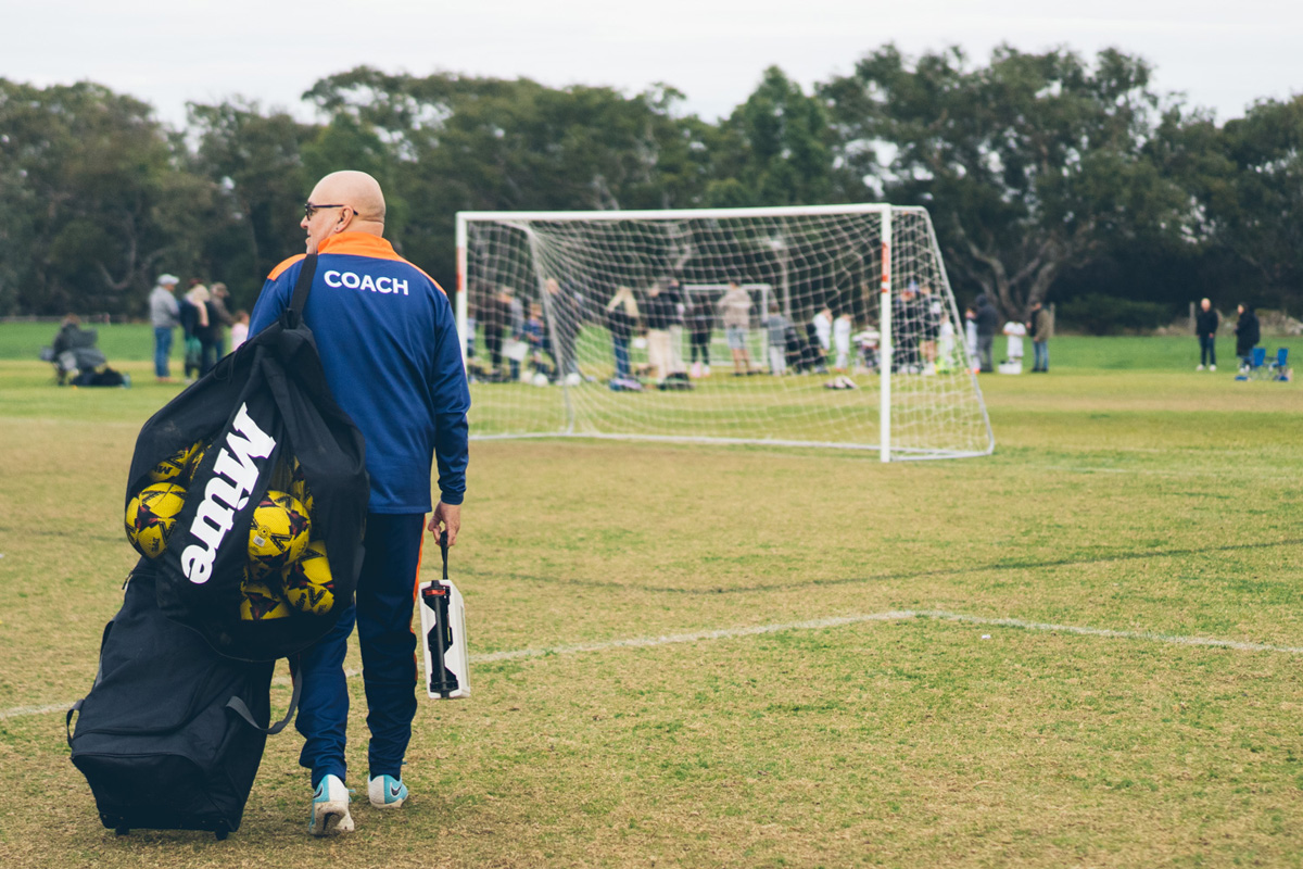 Coach walking across the field with a bag of soccer balls after training