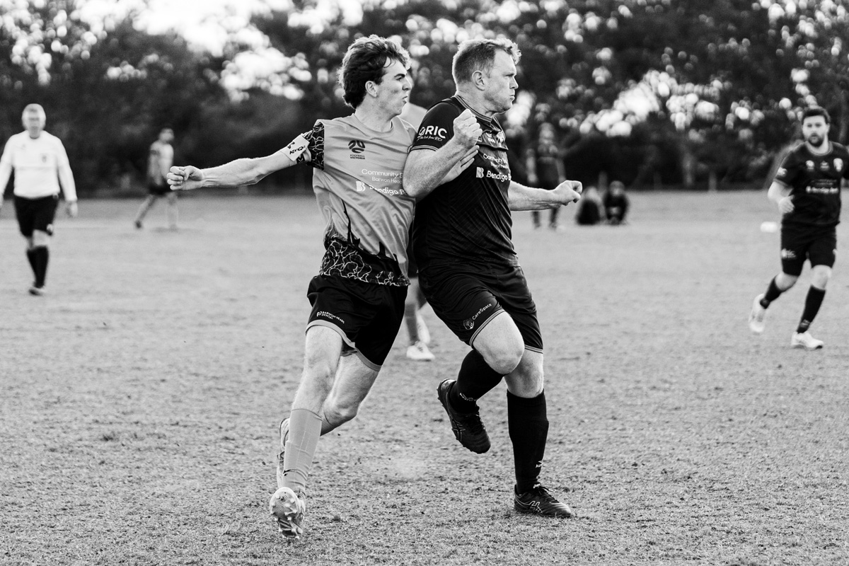 Two adult soccer players contesting the ball mid match from bendigo cup, black and white