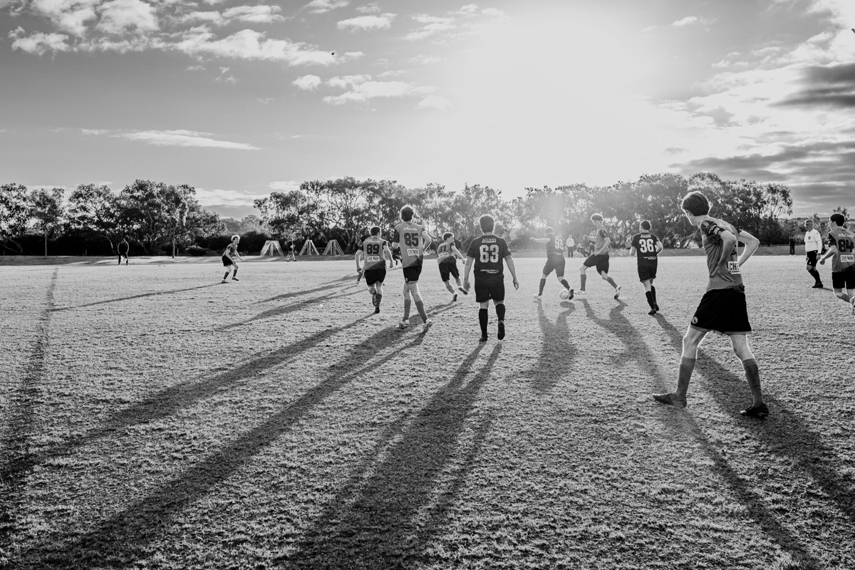 Soccer players running across the field with long shadows in low winter sun, black and white