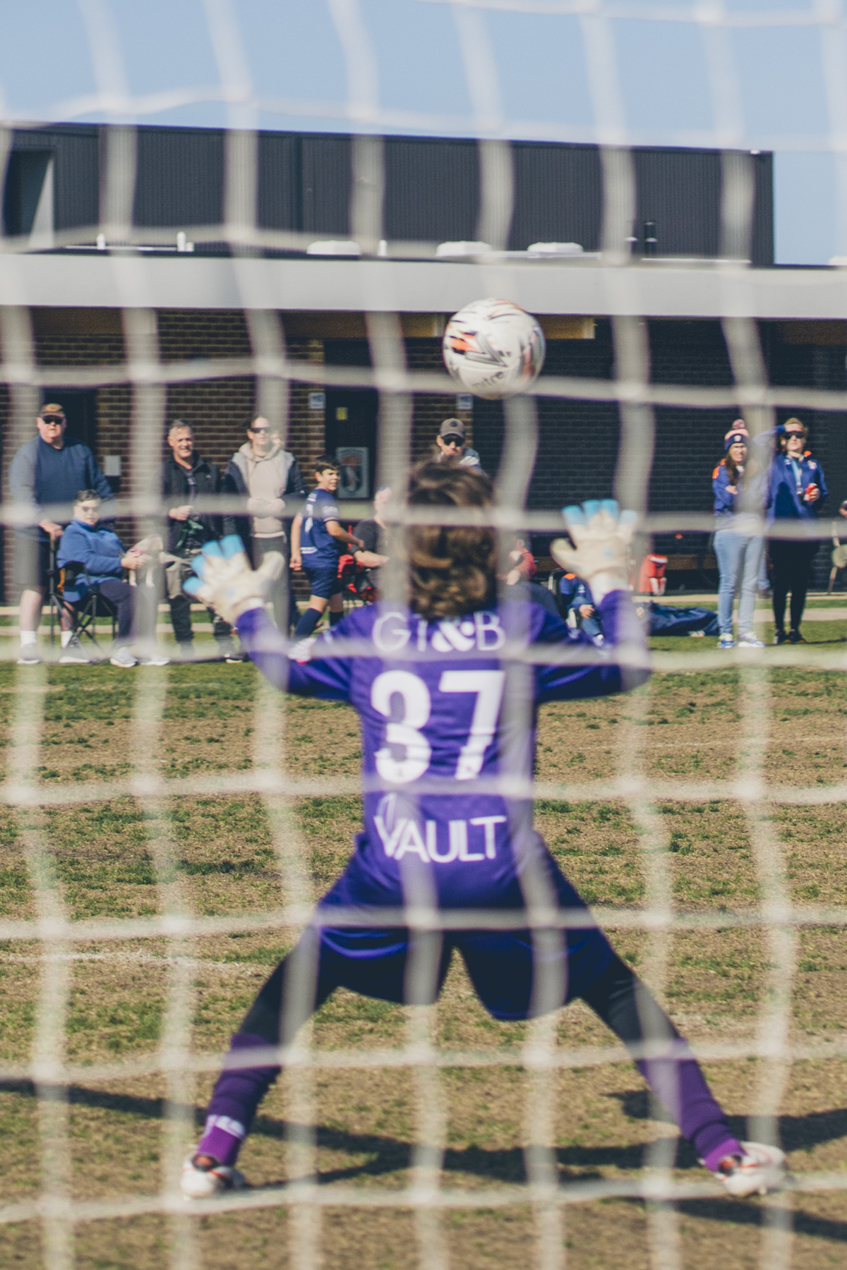 Goalkeeper in purple kit facing an incoming ball, shot through the net