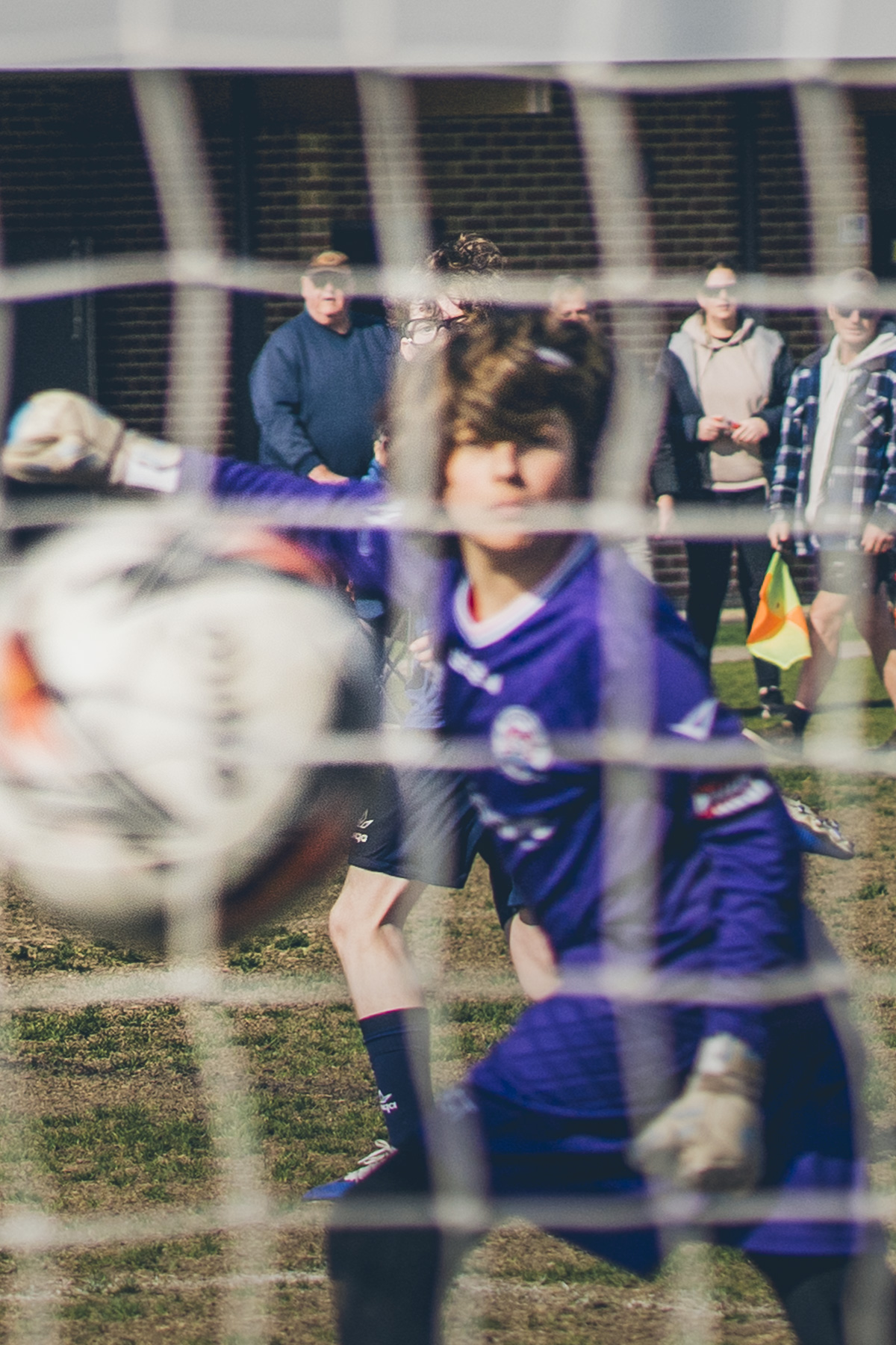 Goalkeeper in purple kit facing an incoming ball, shot through the net