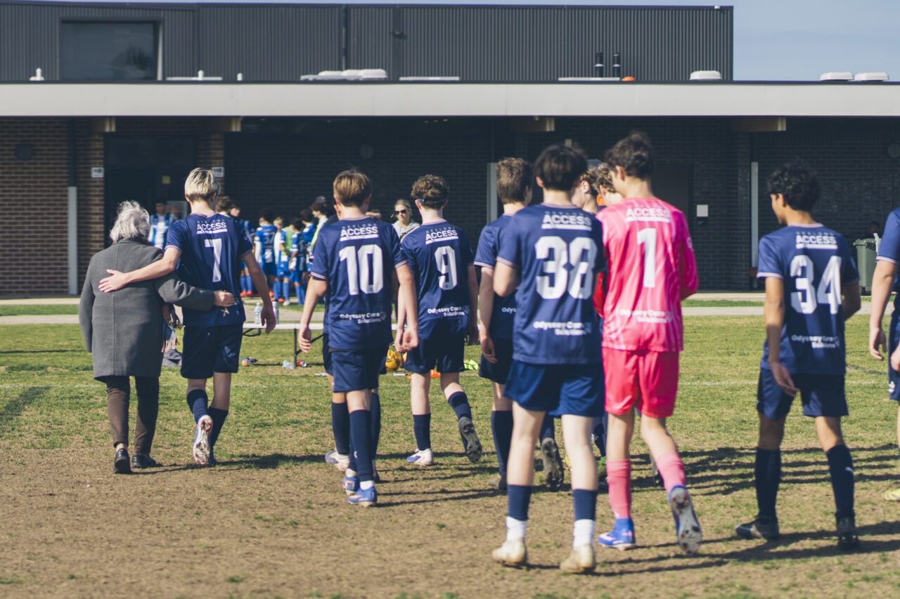Soccer players walking off the field, one with an older woman's arm around him