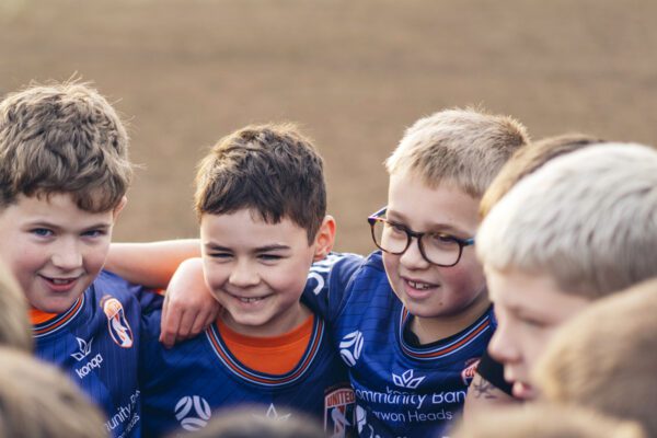 unior soccer players in a team huddle smiling before an AUFC match on the Surf Coast
