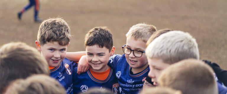 unior soccer players in a team huddle smiling before an AUFC match on the Surf Coast