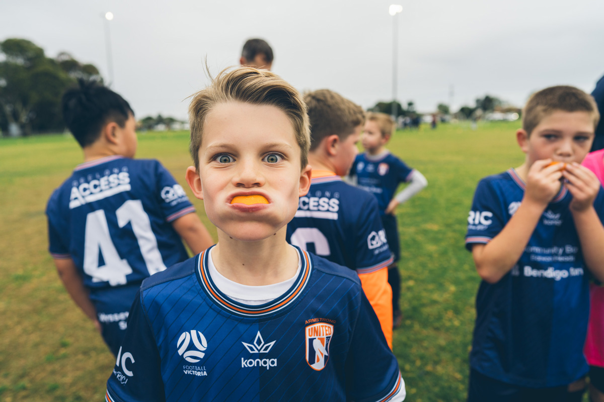 Junior soccer player pulling a funny face with an orange slice in his mouth
