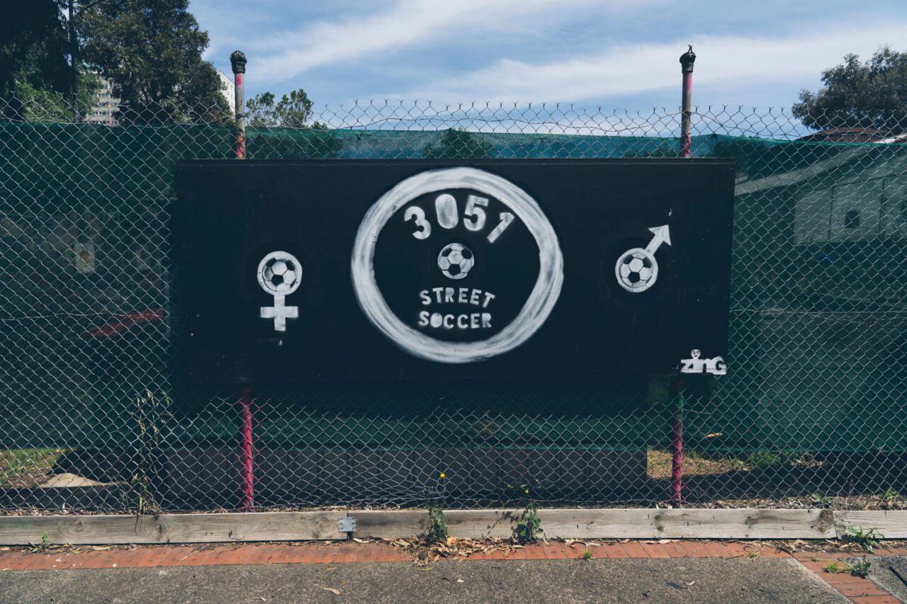 A hand painted 3051 Street Soccer sign on a chain link fence in North Melbourne