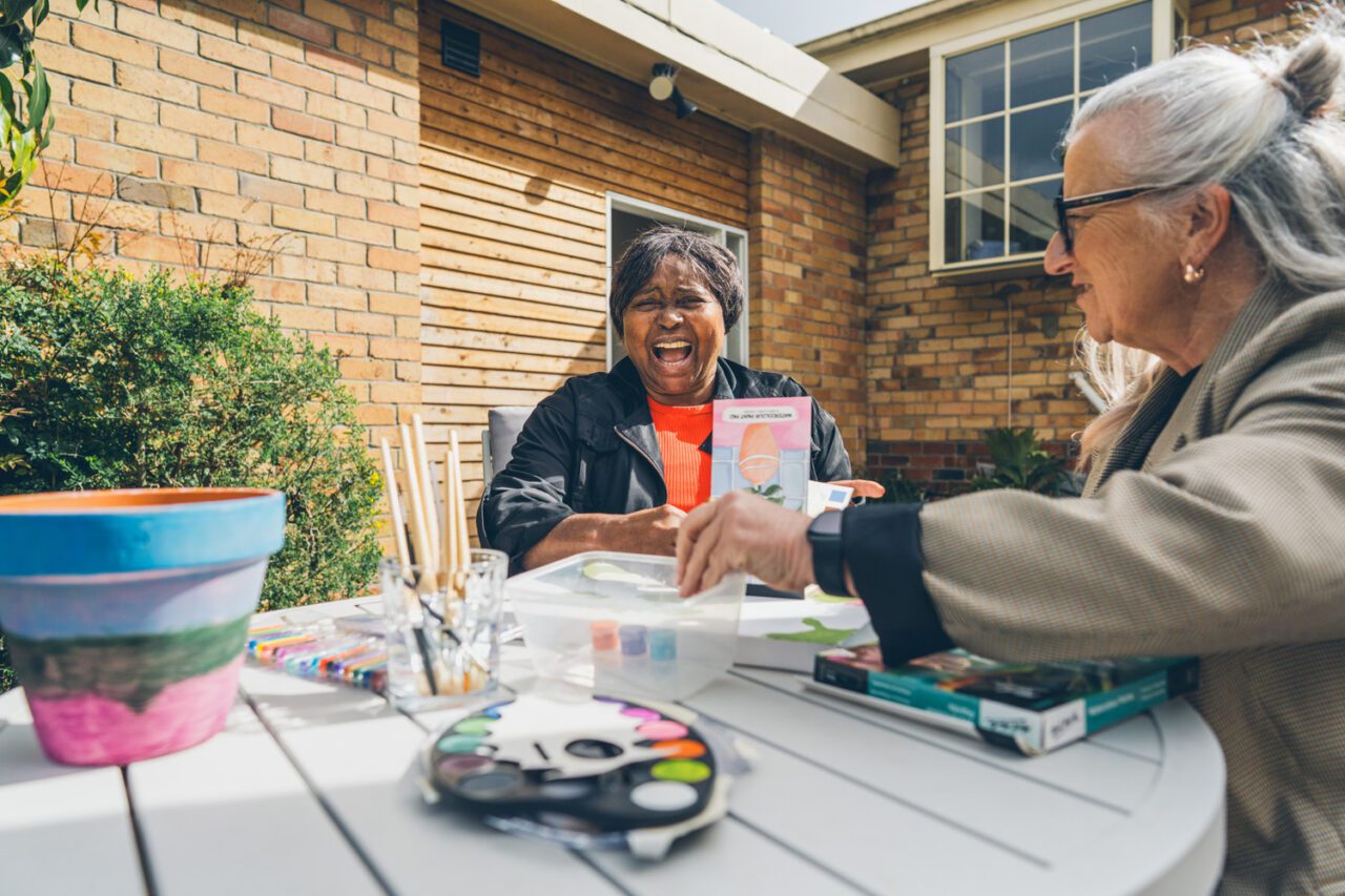 Participant laughing with a support worker during an outdoor watercolour painting session