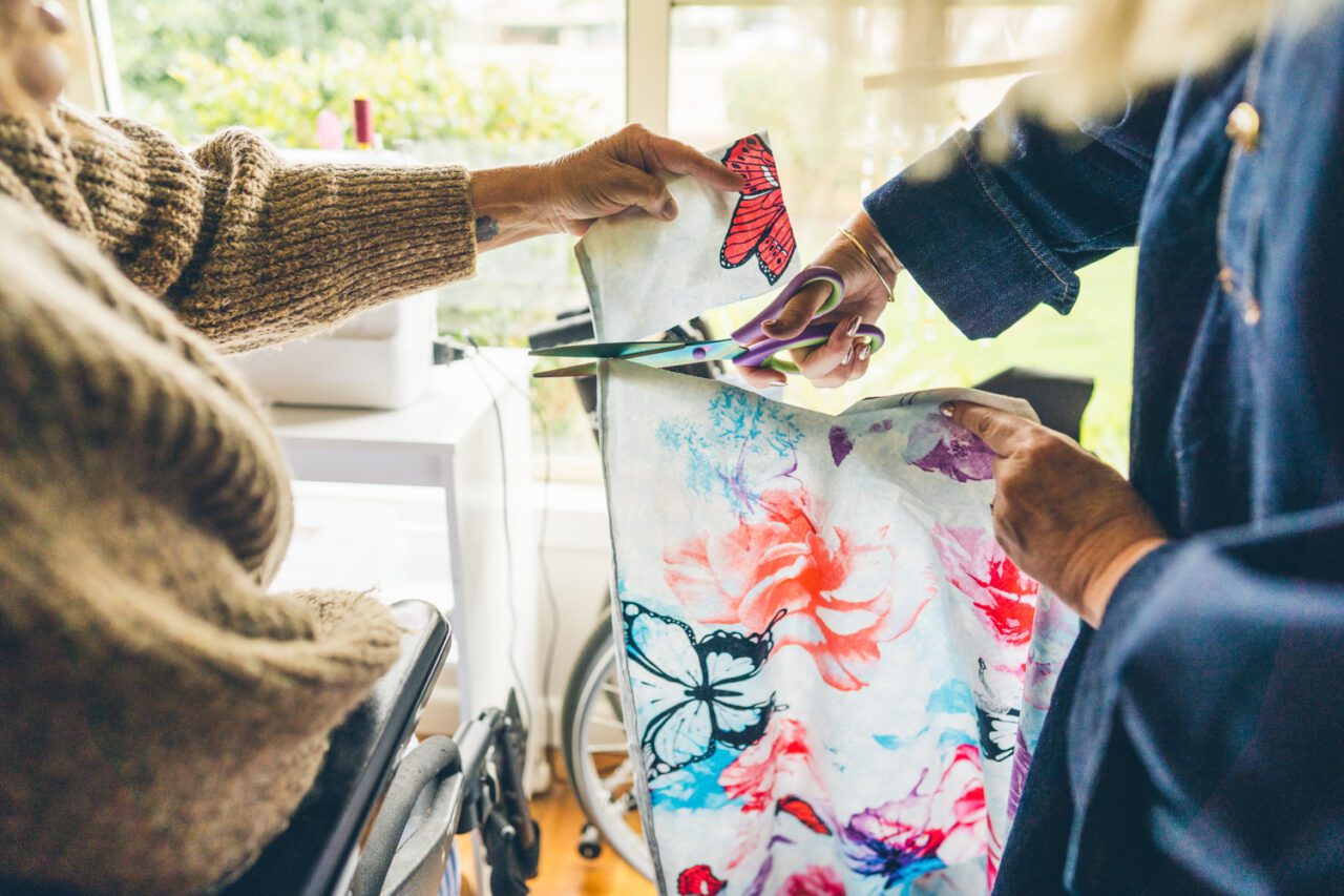 Two people cutting butterfly and floral fabric together with scissors