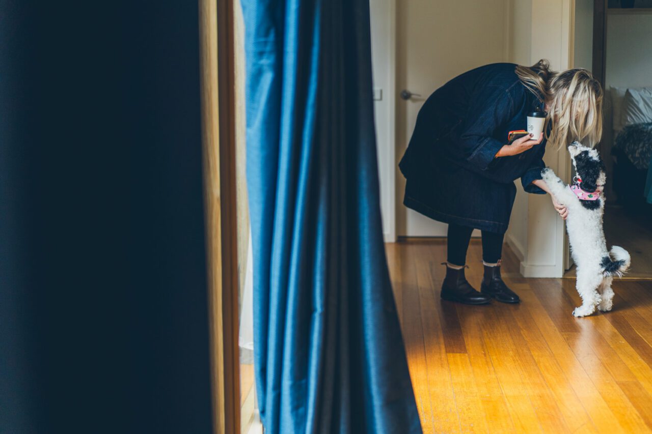 Woman bending down to greet a small black and white dog standing on its hind legs in a hallway
