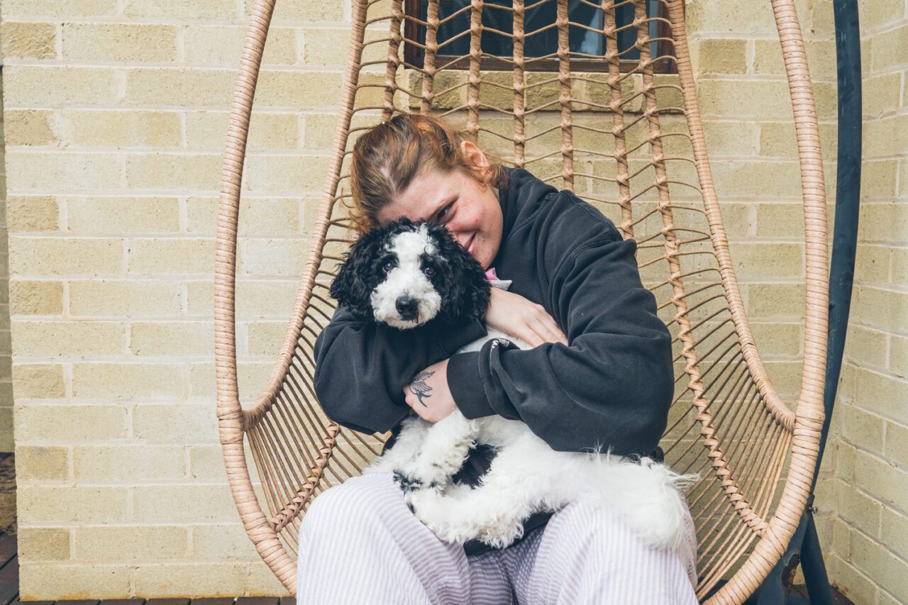 Young woman hugging a black and white puppy in a hanging egg chair