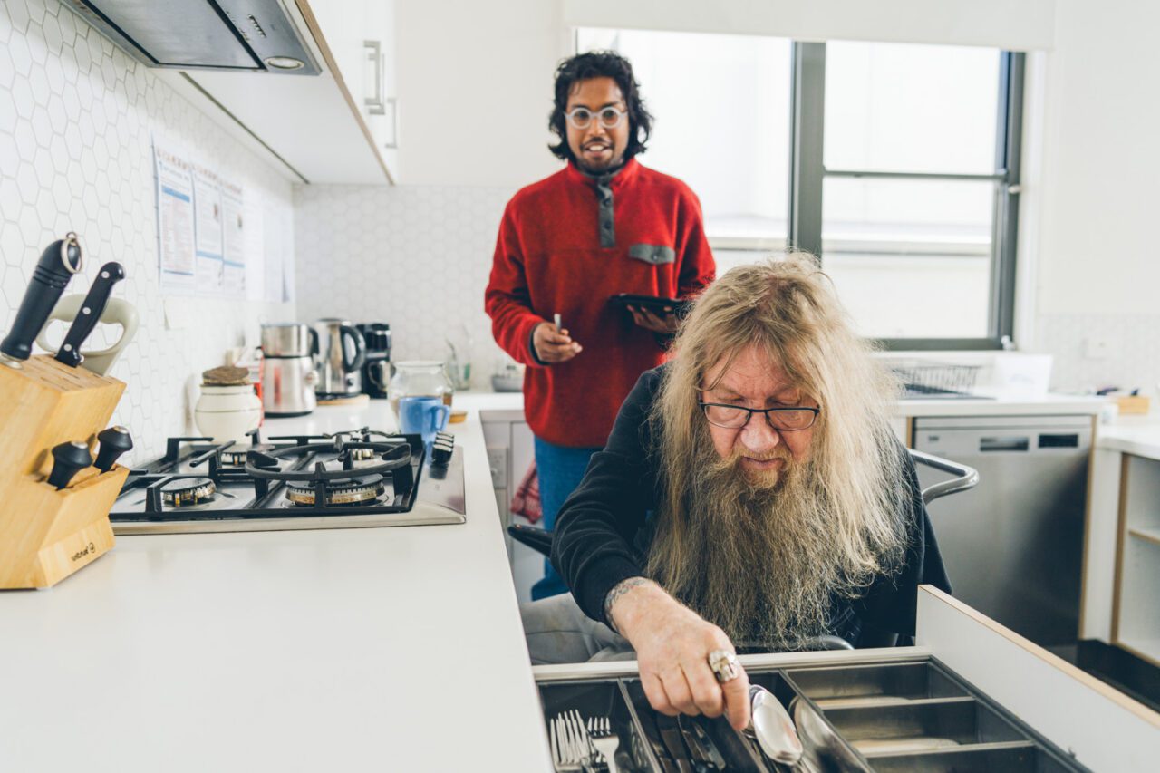 Participant sorting the cutlery drawer in his kitchen with a support worker standing nearby
