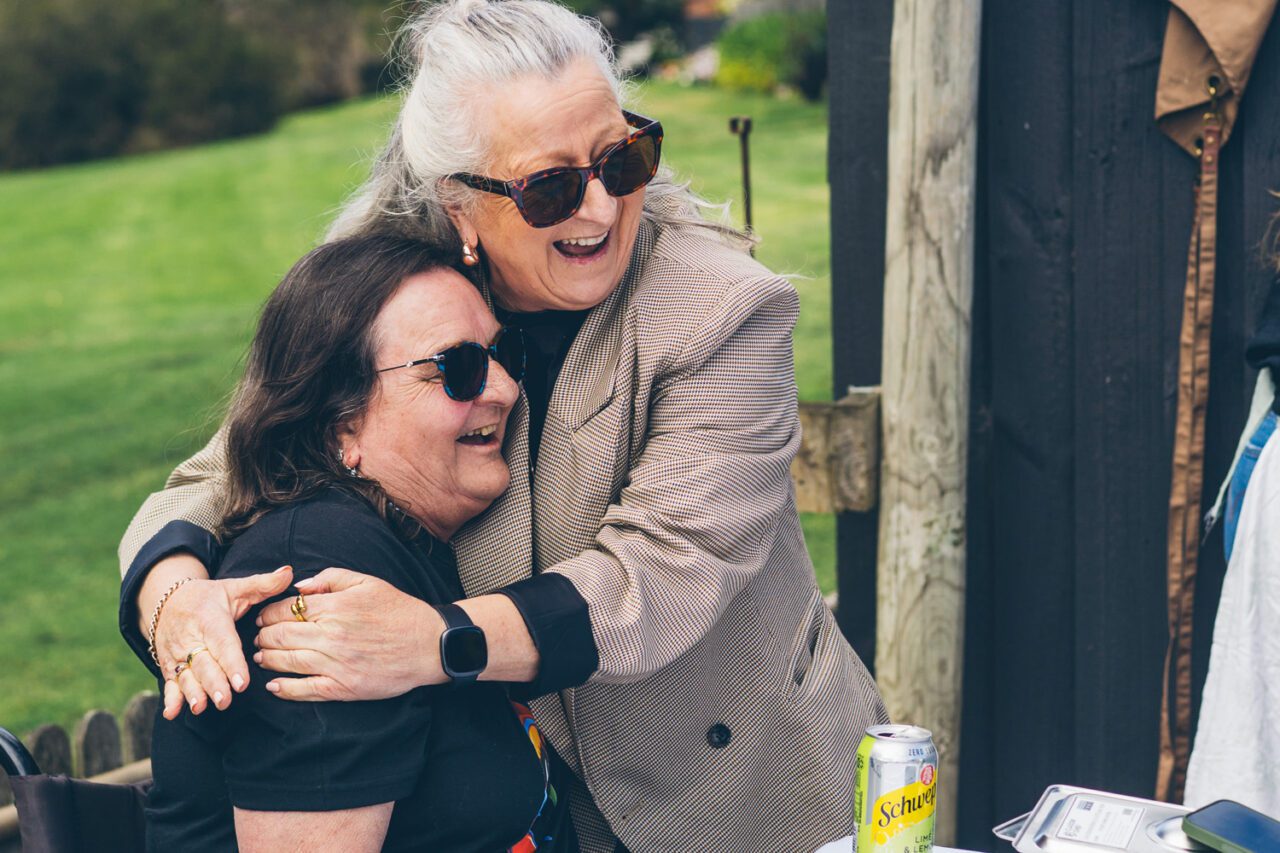 Two women laughing as they hug outdoors in the sun