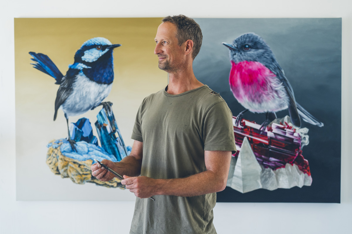 Artist standing in profile beside his bird paintings at Ashmore Arts